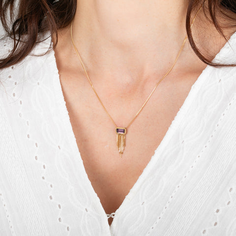 Gold necklace with a a spessartite gemstone adorned with a gold tassel on a person wearing a white top.
