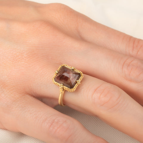A gold ring featuring an Oregon Sunstone gemstone in a 18k gold bezel setting, worn on a person's finger.