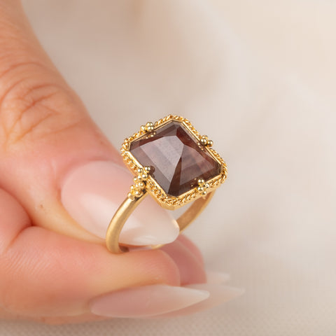 A gold ring featuring an Oregon Sunstone gemstone in a 18k gold bezel setting, held in hand.