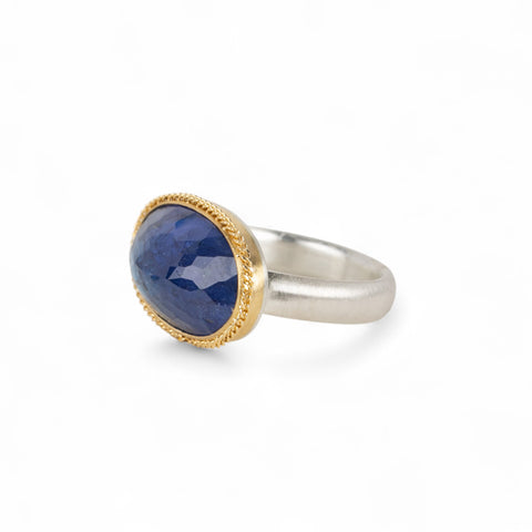 Handmade ring with blue tanzanite, gold bezel and sterling silver band on a white background