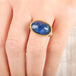 Close up of person wearing a handmade ring with blue tanzanite, gold bezel and sterling silver band on a white background