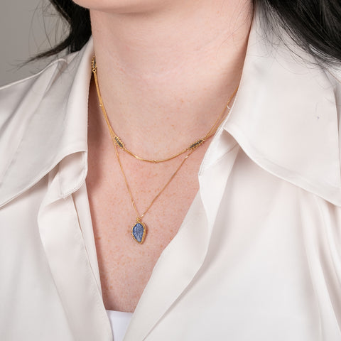 Gold necklace with a leaf-shaped tanzanite pendant on a person.
