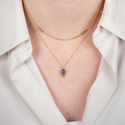 Gold necklace with a leaf-shaped tanzanite on a person