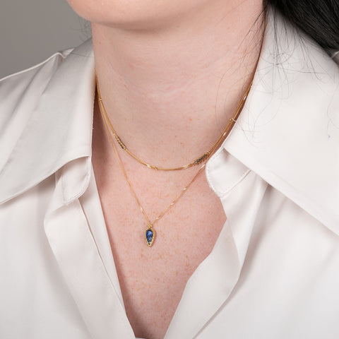Gold necklace with a leaf-shaped tanzanite on a person