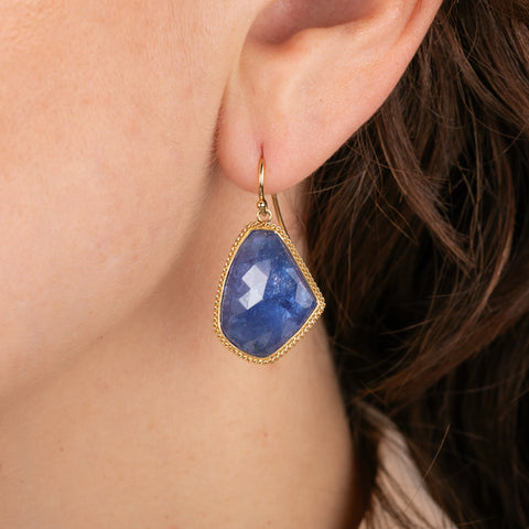 Blue tanzanite earrings with gold settings worn by a person