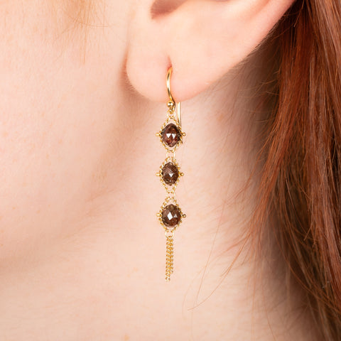 Gold earrings featuring trios of brown diamonds, shown worn in a person's ear.