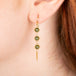 Gold earrings featuring trios of green diamonds, shown worn on a person's ear.