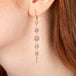 Gold earrings featuring a row of purple Holly Blue Chalcedony stones seen worn on a person's ear