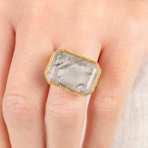 Close up of a person wearing a handmade fine jewelry tourmalated quartz ring in 18k gold and sterling silver