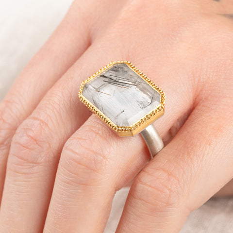 Close up of a person wearing a handmade fine jewelry tourmalated quartz ring in 18k gold and sterling silver