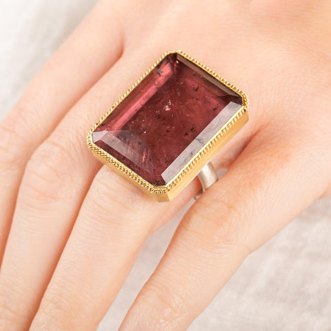 A close up of a person wearing a handcrafted ring with a tourmaline gemstone, 18k gold bezel and sterling silver band