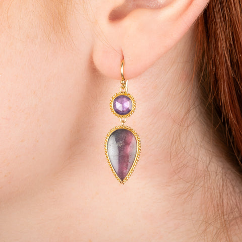 Gold drop earring featuring watermelon tourmaline and lavender sapphire gemstones, shown worn in a person's ear.