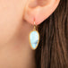 A close-up of a gold dangle earring with a light blue turquoise stone, shown worn on a person's ear.