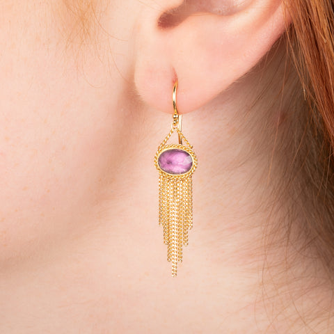Gold earrings featuring vibrant umbalite garnet gemstones, shown worn in a person's ear.