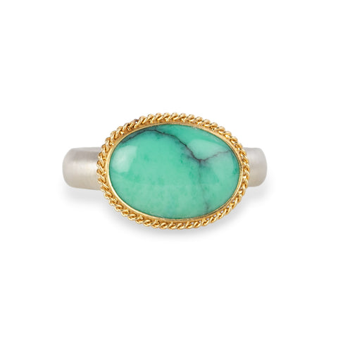An oval ring featuring a green variscite stone with a natural matrix, set in a gold bezel with a sterling silver band on a white background
