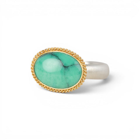 An oval ring featuring a green variscite stone with a natural matrix, set in a gold bezel with a sterling silver band on a white background