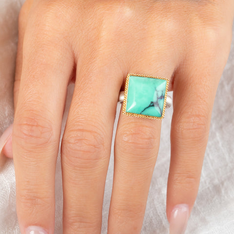 A gold and silver ring featuring a Variscite stone worn on a finger.