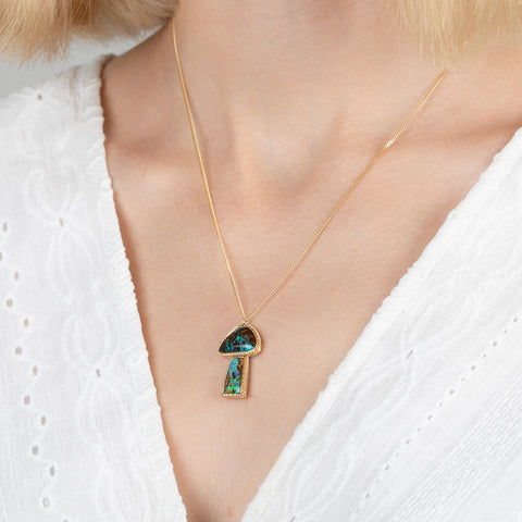 Gold mushroom necklace with a colorful boulder opal pendant on a person wearing a white top.