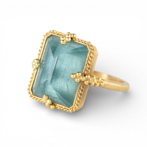 Gold ring with a rectangular aquamarine gemstone on a white background