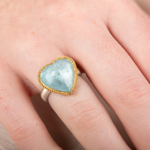 Heart-shaped ring with aquamarine stone, gold bezel and silver band on a hand