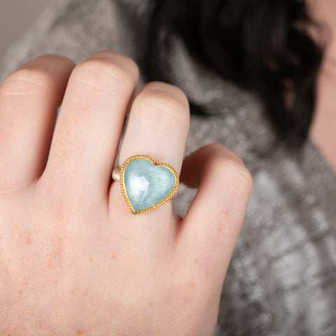 Heart-shaped ring with aquamarine stone, gold bezel and silver band on a person's hand