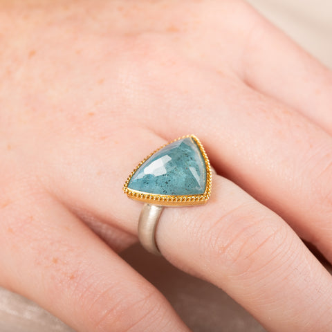 Aquamarine stone ring with gold setting and silver band on a person's finger