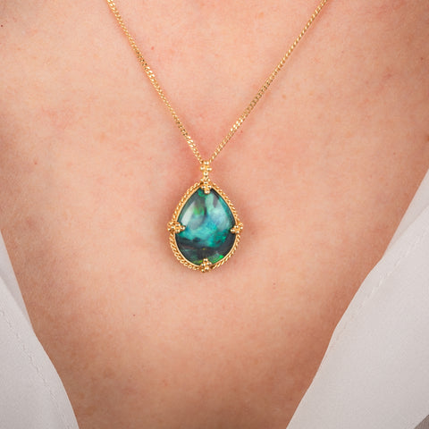 Gold necklace with a black opal teardrop pendant on a person's neck