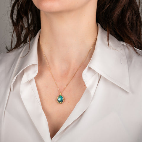 Gold necklace with a black opal teardrop pendant on a person's neck