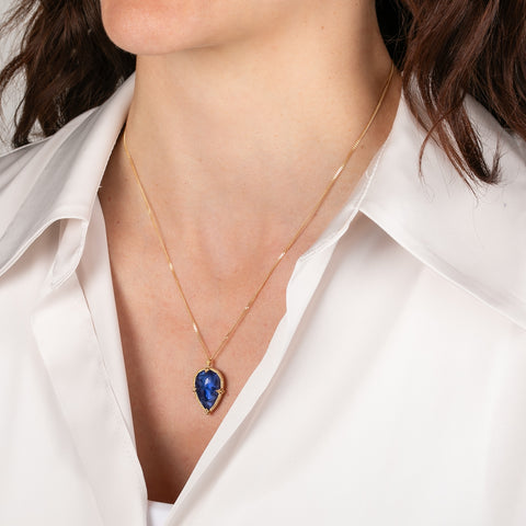Gold necklace with a blue teardrop-shaped tanzanite gemstone pendant on a person