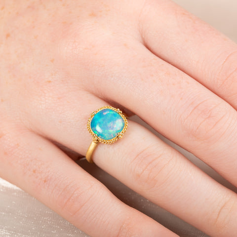 Gold ring with an Ethiopian opal stone on a person's finger