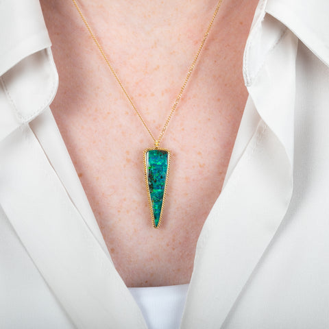 Triangle-shaped boulder opal stone pendant with a gold setting on a person