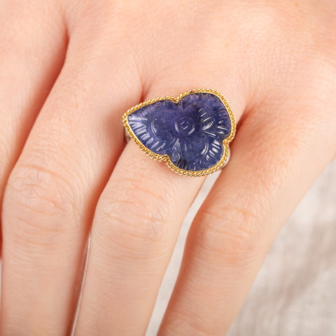 A person wears a handmade fine jewelry ring with carved tanzanite stone set in gold and complete with sterling silver band