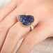 A person wears a handmade fine jewelry ring with carved tanzanite stone set in gold and complete with sterling silver band