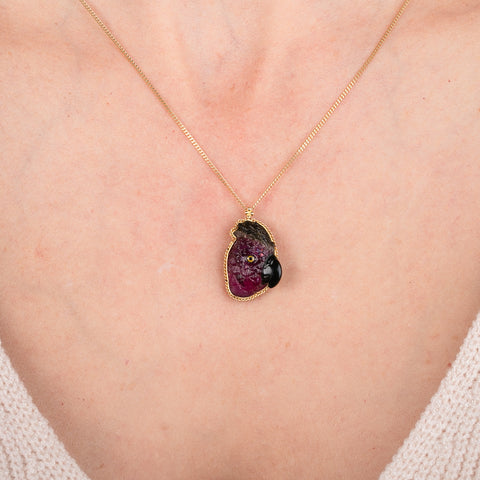Gold necklace featuring a carved tourmaline parrot pendant on a person's neck