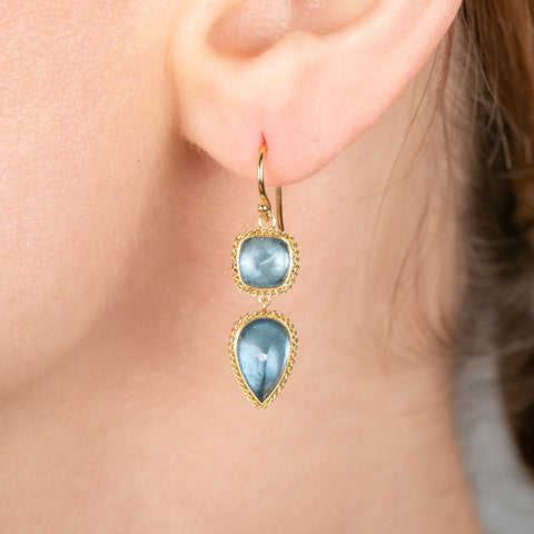 Gold earrings with blue aquamarine gemstones worn by a person