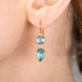 Gold earrings with blue aquamarine gemstones worn by a person