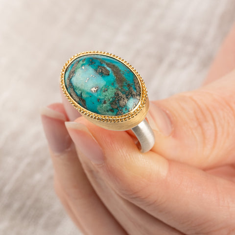 A close up of a person holding a handmade fine jewelry turquoise ring with an 18k gold bezel and sterling silver band