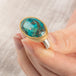 A close up of a person holding a handmade fine jewelry turquoise ring with an 18k gold bezel and sterling silver band