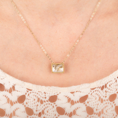 Gold necklace with a rectangular dendritic quartz pendant worn by a person wearing a lace top.