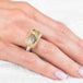 Gold and silver ring with a rectangular, dendritic quartz stone on a hand against a white background