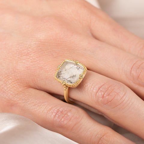 Gold ring with a dendritic quartz stone on a person's finger