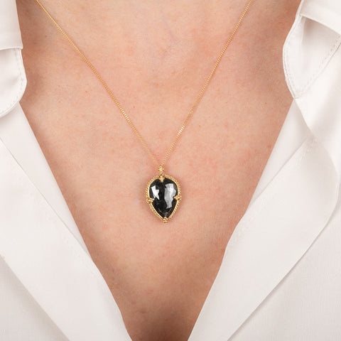 Gold necklace with a black diamond pendant on a white shirt