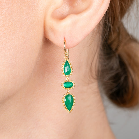 Emerald trio earrings with gold bezels worn by a person.