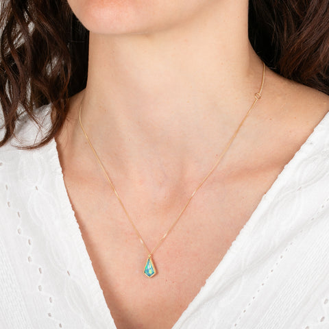 Gold necklace with an Ethiopian opal pendant worn by a person against a white background