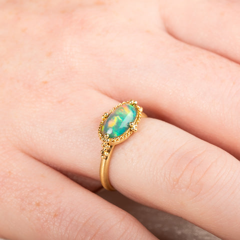 Gold ring with an Ethiopian opal stone on a person's finger