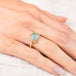 Gold ring with a light blue aquamarine gemstone on a hand against a white background