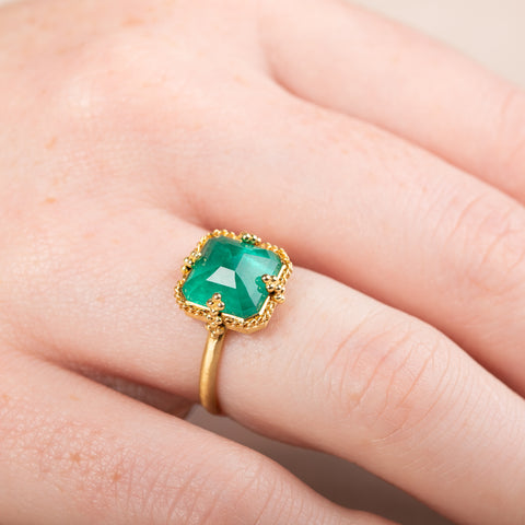 Gold ring with an emerald gemstone worn on a finger