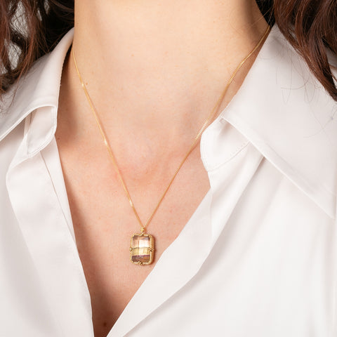 Gold necklace with a fluorite pendant worn by a person in a white shirt