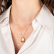 Gold necklace with a fluorite pendant worn by a person in a white shirt