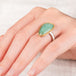 Hand wearing a ring featuring an emerald gemstone set in an 18k gold bezel with a silver band